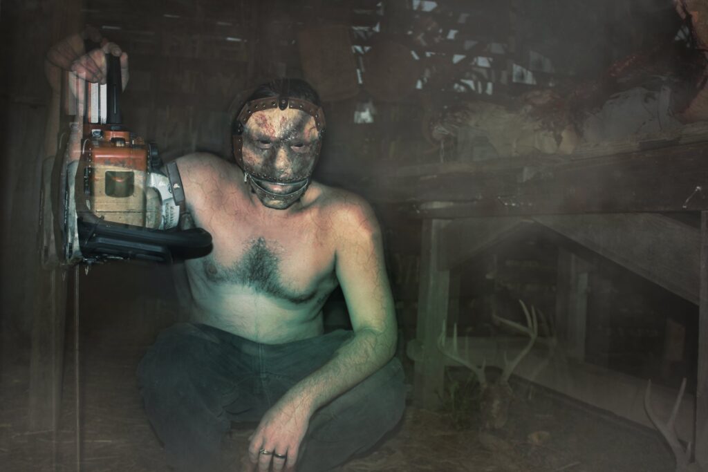 A Field of Screams character holding a chainsaw inside the dark haunted barn.