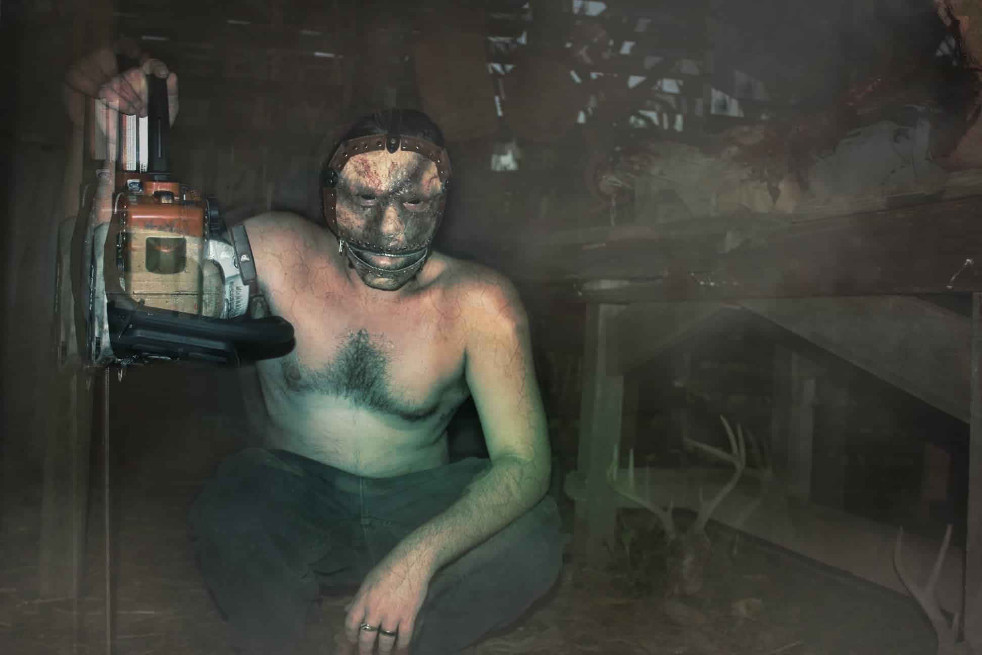 A Field of Screams character holding a chainsaw inside the dark haunted barn.