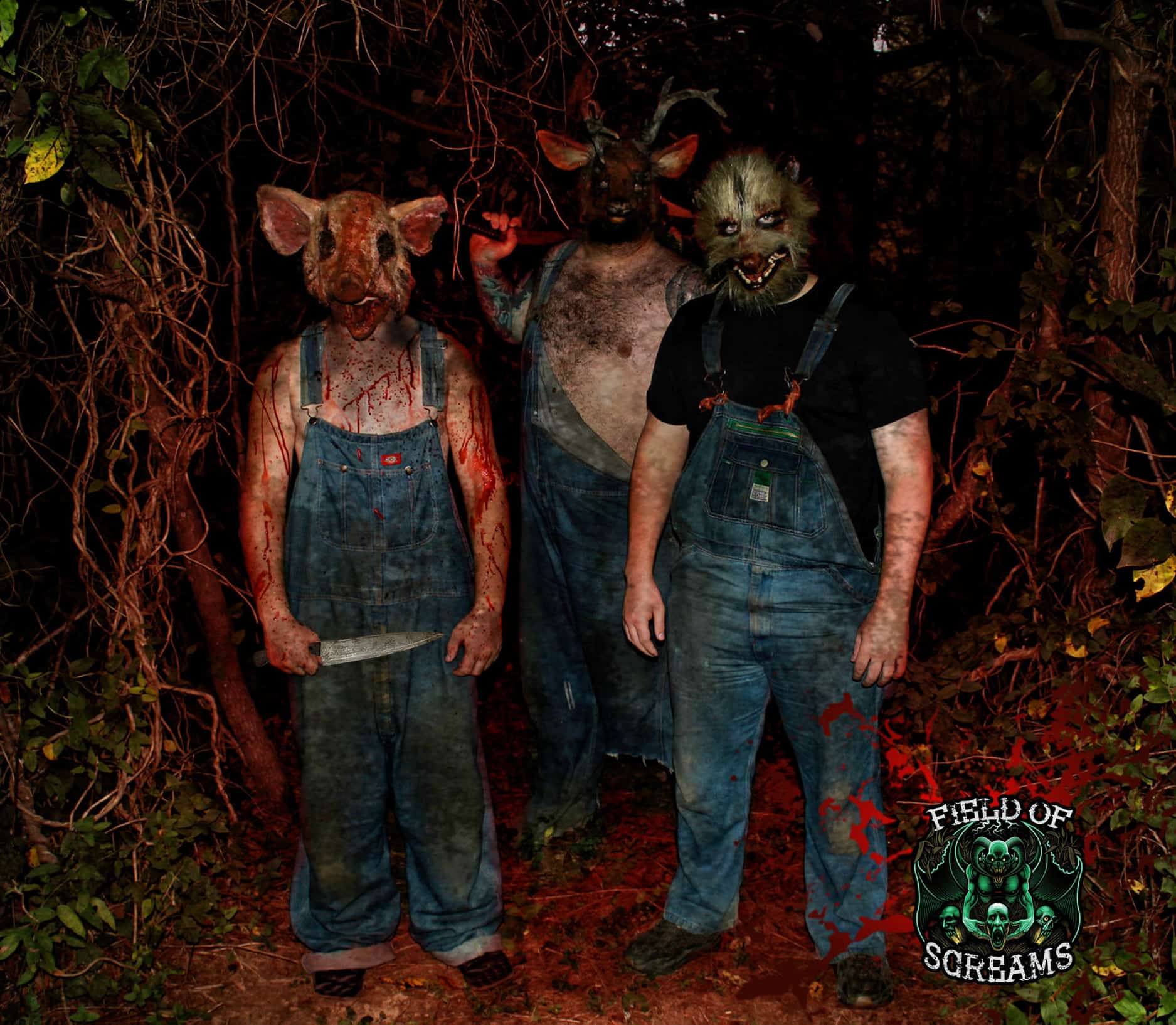 Three masked Field of Screams characters in overalls standing among the trees at night.